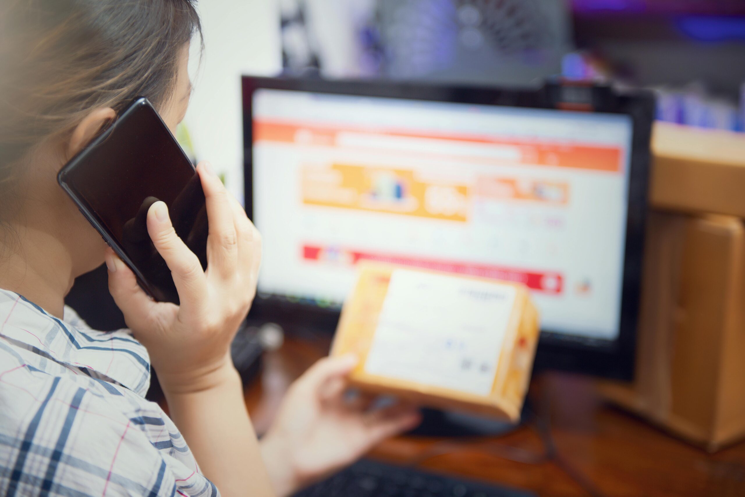 Frau erledigt mehrere Dinge gleichzeitig, indem sie zu Hause ein Telefon benutzt und ein Online-Kaufpaket prÃ¼ft.